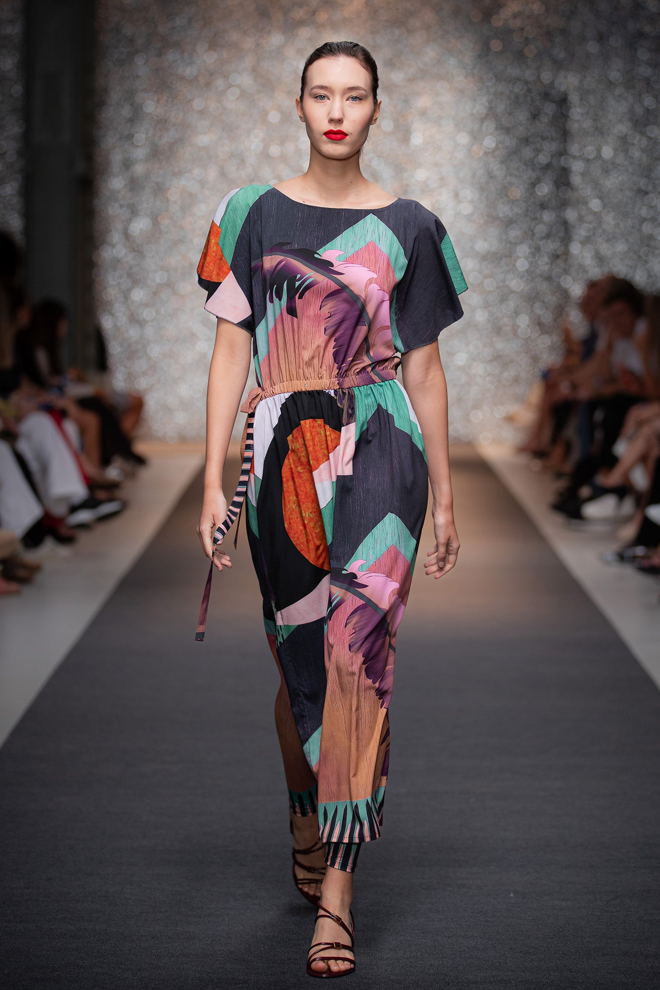 Model walking on a runway wearing a colorful dress with abstract patterns.