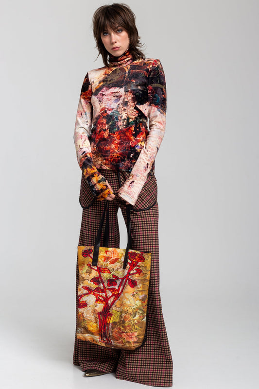A person holding a multicolored tote bag with a floral and abstract design.
