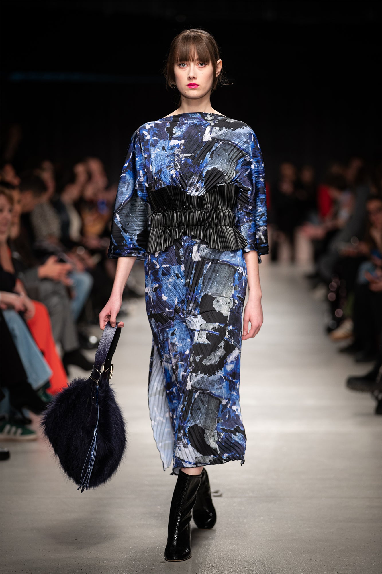 Model walking on a runway wearing a blue abstract patterned pleated midi dress.