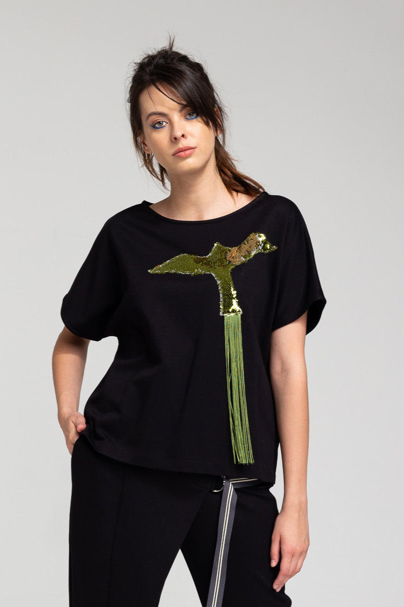 A woman wearing a black top with a sequined, fringe tailed bird design on the front.
