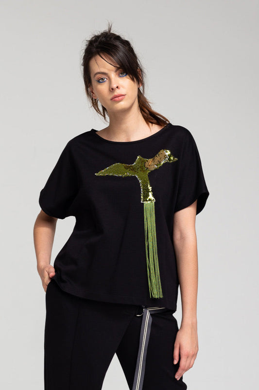 A woman wearing a black top with a sequined, fringe tailed bird design on the front.