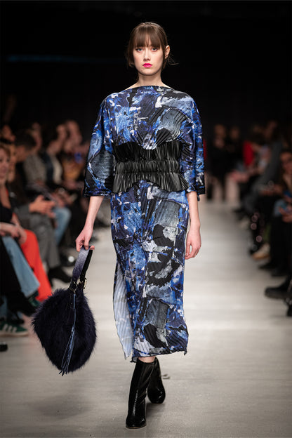 Model walking on a runway wearing a blue abstract patterned pleated midi dress.