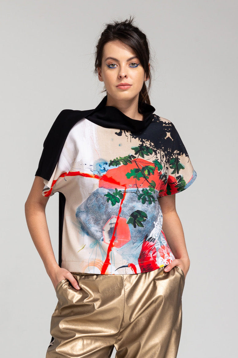 A model wearing an asymmetric neckline top with a printed front. The print includes artistic brush strokes in various colors.